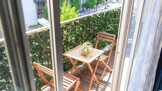 A wooden table and chairs on a balcony with a view of greenery and buildings. - Dai 40 prosper Apartment (Nagoya)