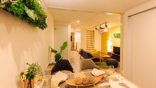 A modern dining area with a table set for two, a sofa, and a TV in the background. - ORIGAMI STAY -Taishocho- (Nagoya)