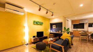 A modern living room with a sofa, TV, and a dining area with a kitchen in the background. - ORIGAMI STAY -Taishocho- (Nagoya)