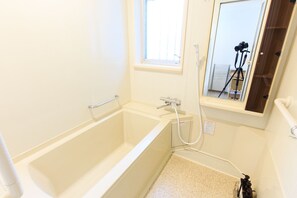 Une petite salle de bain blanche avec une baignoire, une fenêtre et un trépied pour appareil photo à l’arrière-plan.