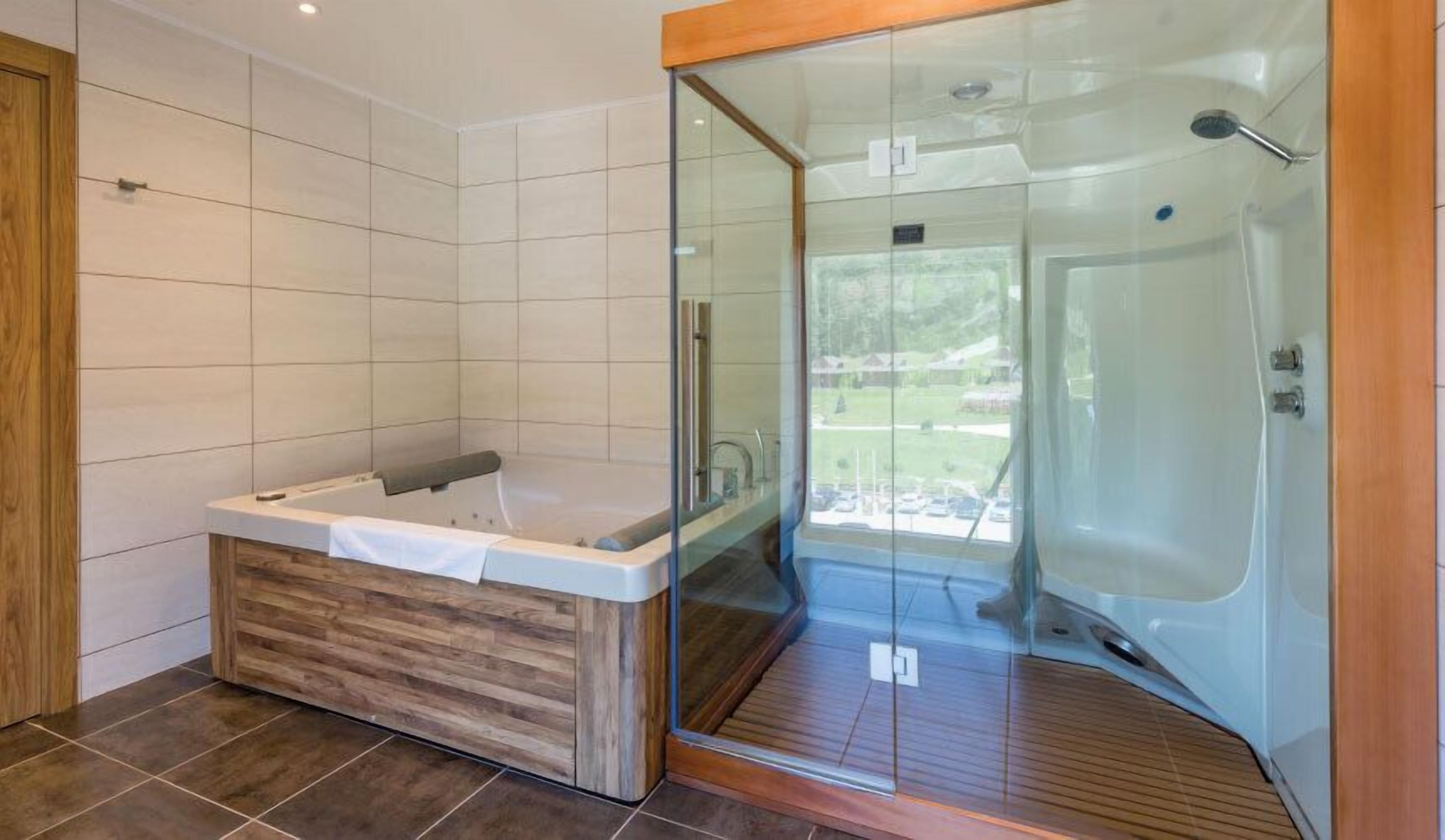 A modern bathroom with a wooden bathtub, a glass-enclosed shower, and a view of the outdoors.