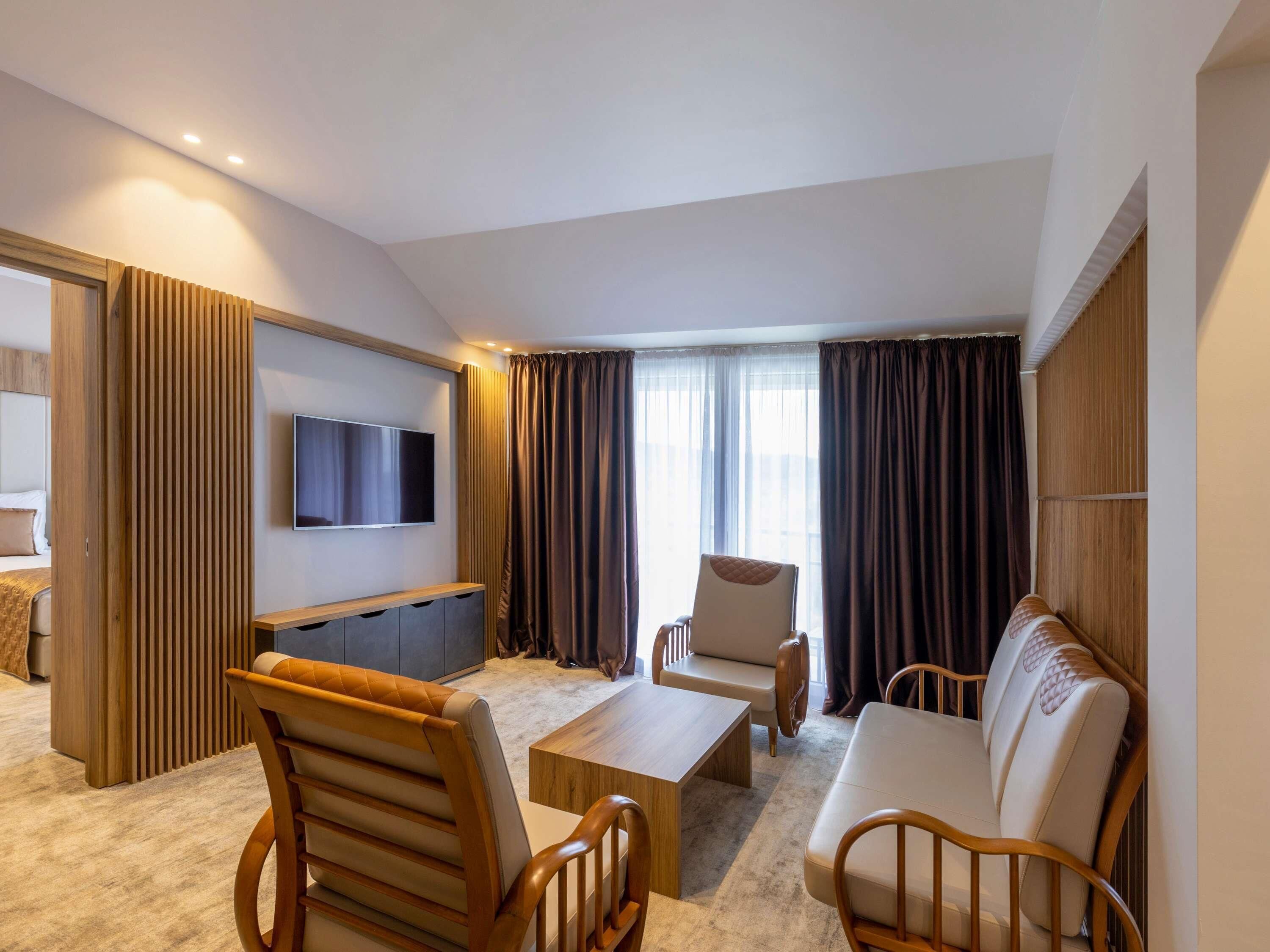 A modern hotel room with a sofa, chairs, a TV, and a wooden partition.
