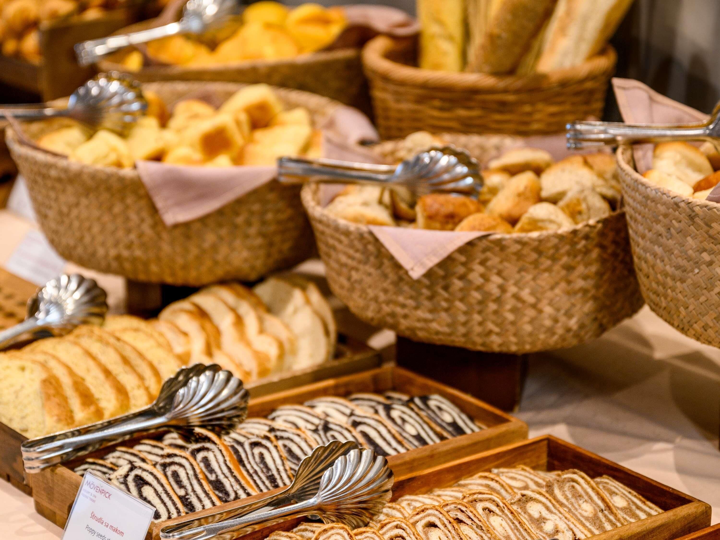 Variedad de productos horneados expuestos en cestas y bandejas de madera, como pan, pasteles y tortas.