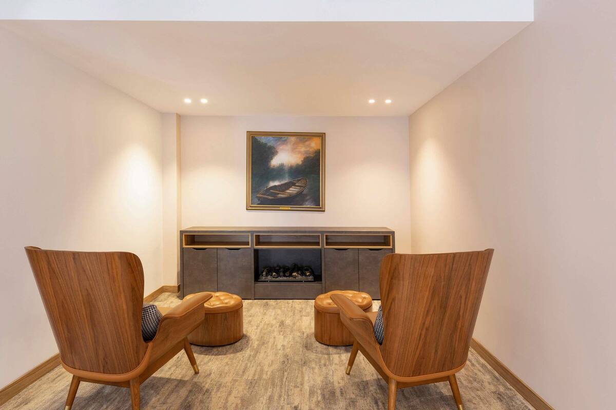 A modern living room with two wooden chairs, a fireplace, and a framed painting on the wall.