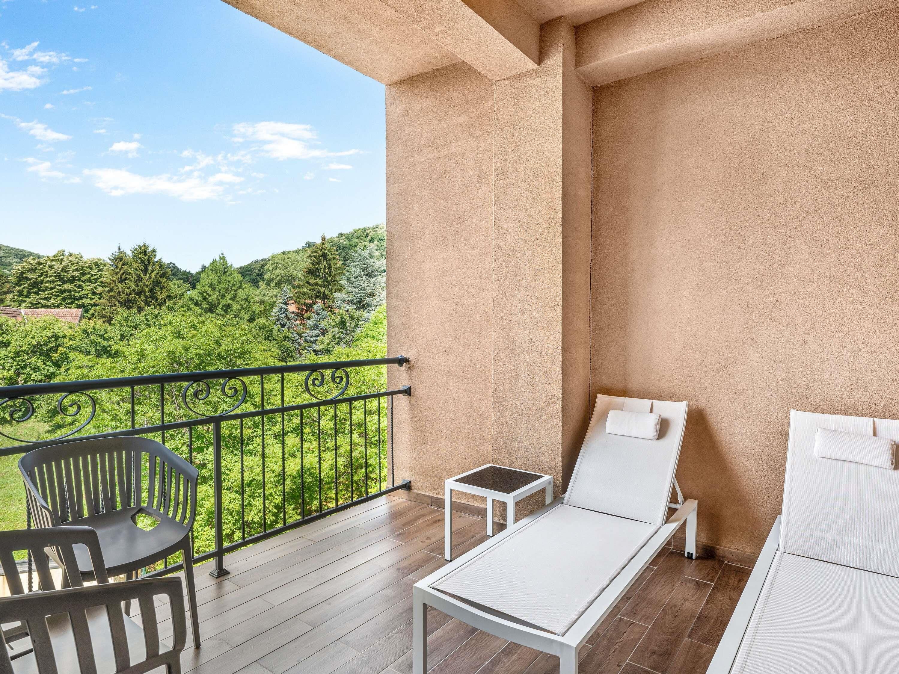 A balcony with a wooden floor, a white sofa, a small table, and a chair.