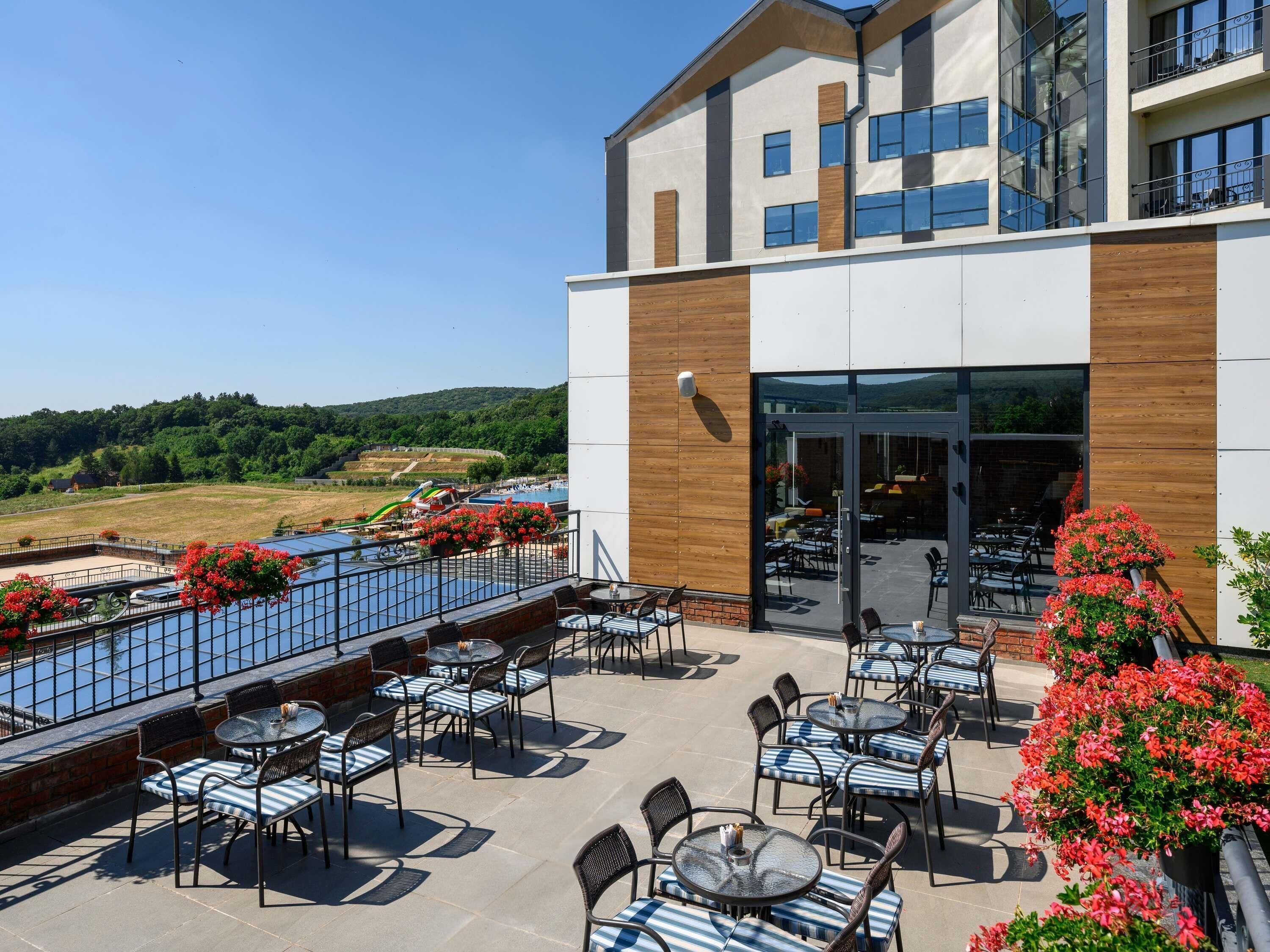 A modern building with a pool, outdoor seating, and a view of the landscape.