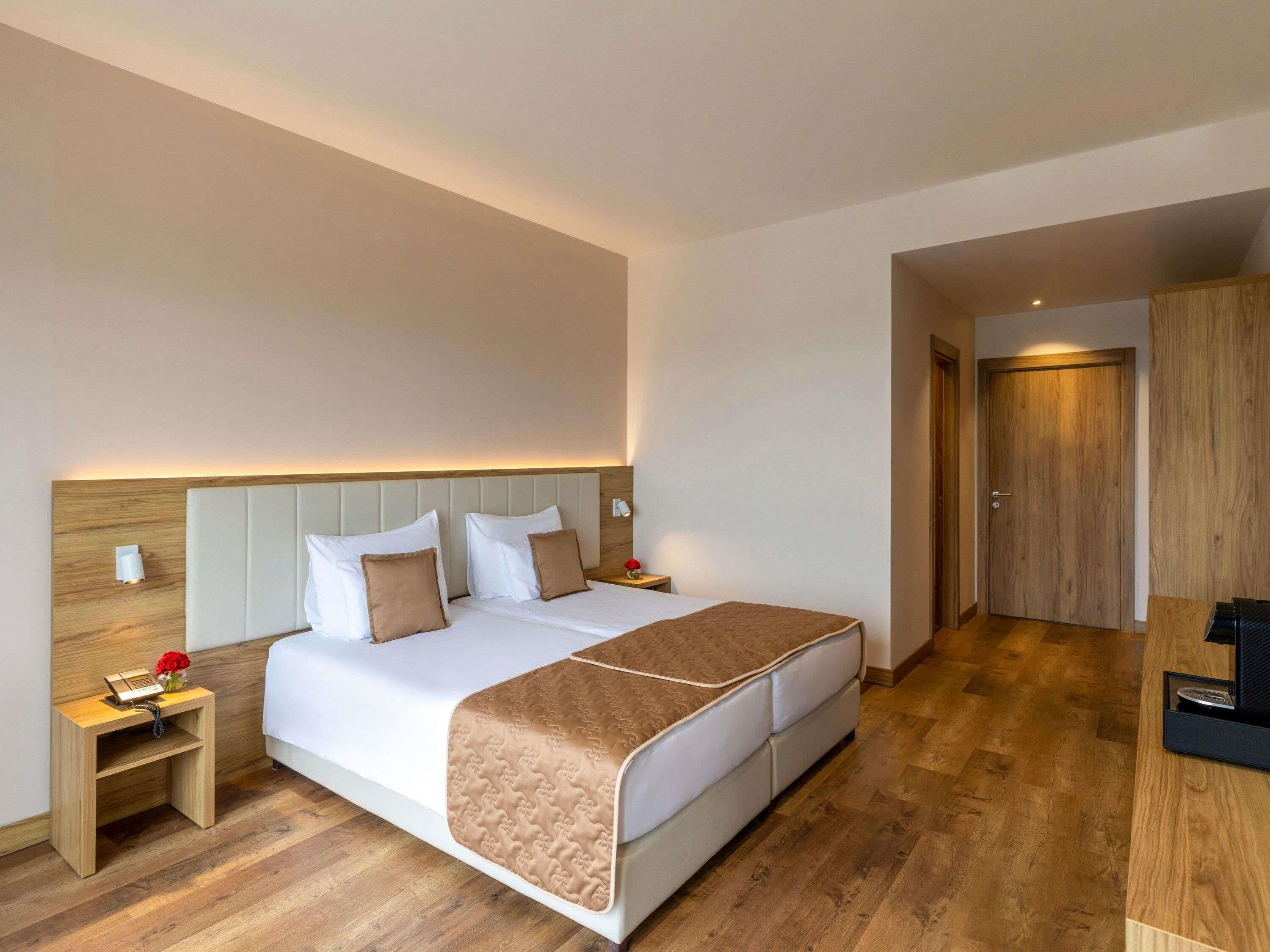 A hotel room with a bed, bedside tables, a desk, and a wooden door.