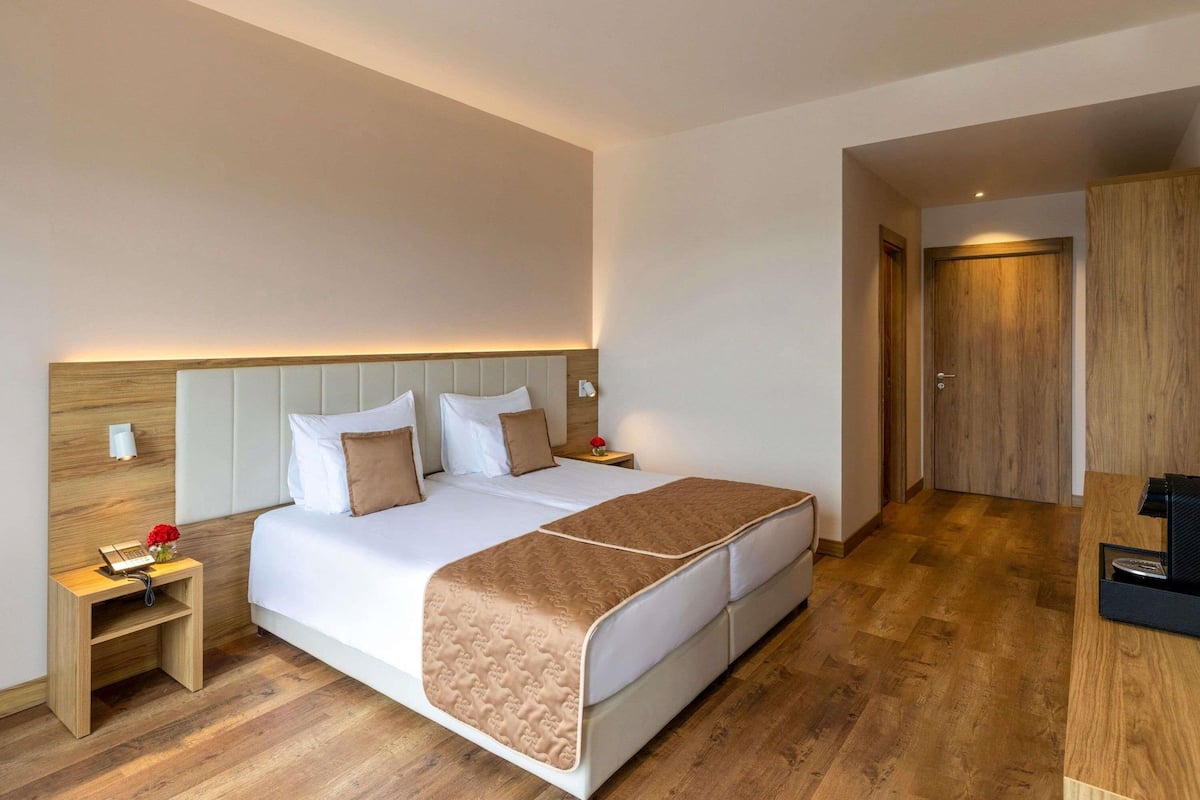 Ein Hotelzimmer mit Bett, Nachttischen, einem Schreibtisch und einer Holztür.