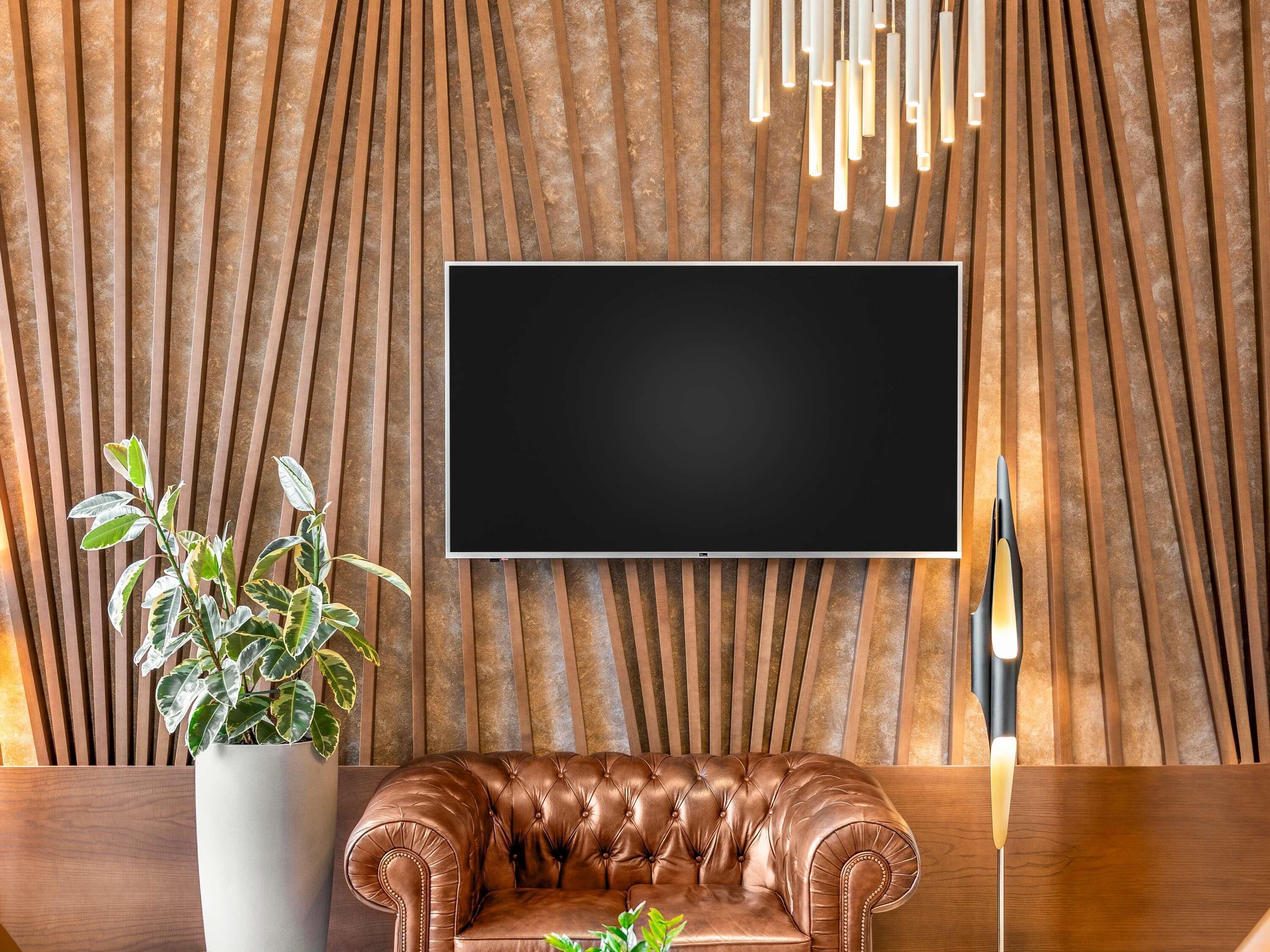 Un salon moderne avec un canapé en cuir, un grand téléviseur à écran plat fixé sur un mur texturé et une plante en pot.