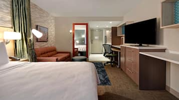A hotel room with a bed, a desk with a TV, a chair, a desk lamp, and a window with curtains.