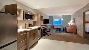 Una habitación de hotel moderna con kitchenette, un escritorio, un sofá cómodo y un ventanal grande.