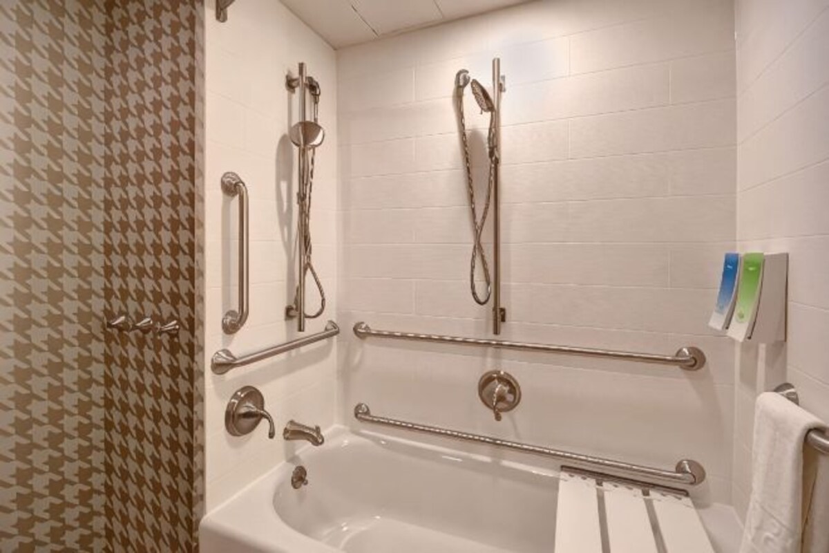 A bathroom with a white bathtub, grab bars, and a shower with a handheld showerhead.