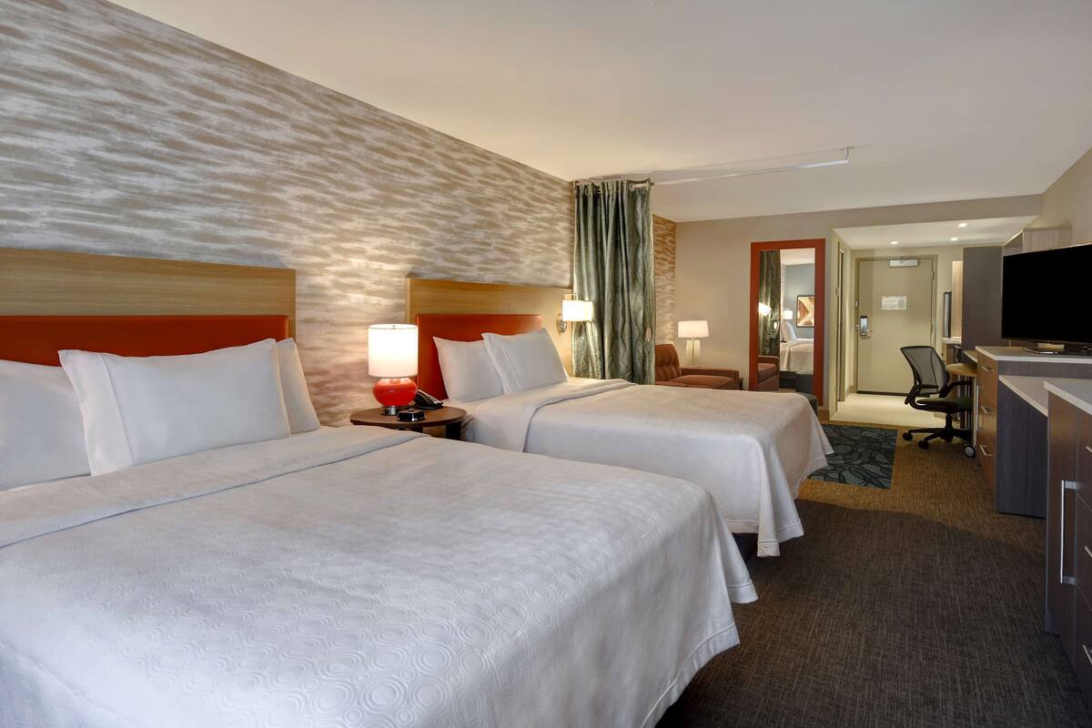 A hotel room with two beds, a desk, a TV, and a bathroom visible through an open door.