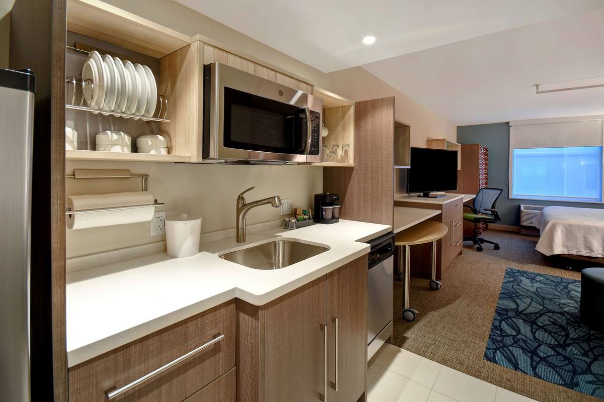 A modern kitchen with stainless steel appliances, a sink, and a dining area with a TV and a bed.