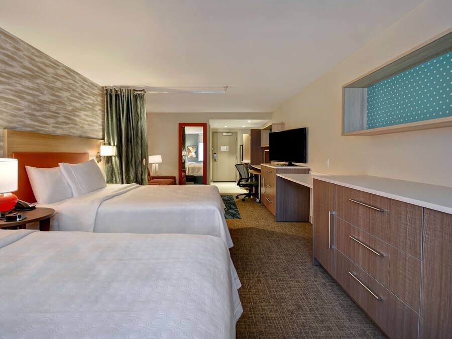 A hotel room with two beds, a desk, a TV, and a bathroom visible through an open door.
