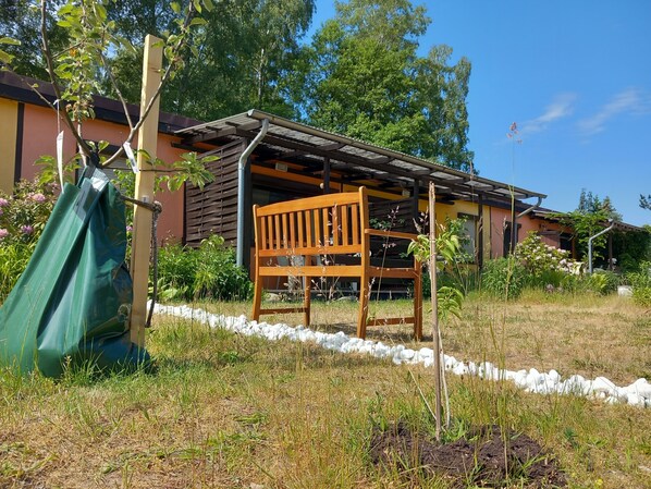 A wooden bench in a garden area with a building in the background. - Last Minute Juni Angebot!  (Joachimsthal)