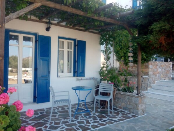 Un área de estar al aire libre techada, con suelo de piedra, contraventanas azules y paredes blancas.