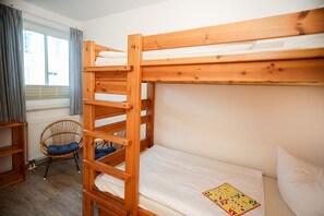 Ein Etagenbett mit einer Leiter, ein Stuhl mit Kissen sowie ein Fenster mit Vorhängen.