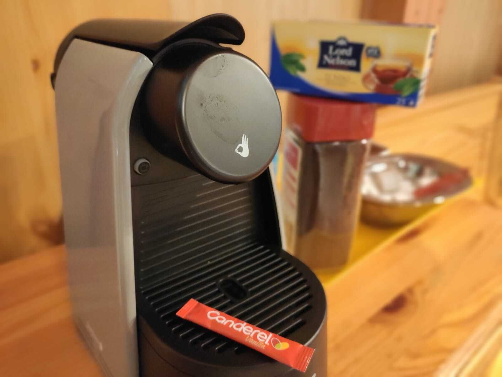 A coffee machine with a single pod inserted, a container of coffee creamer, and a box of instant coffee in the background.