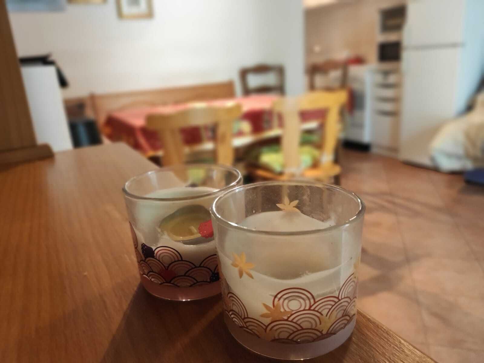 Two glasses with a floral design on a wooden table in a room with a dining area in the background.