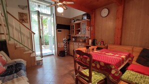 Una camera accogliente con soffitto in legno, un tavolo da pranzo con sedie, un letto con copripiumino a quadretti rossi e verdi, e una scala che conduce a una zona esterna.