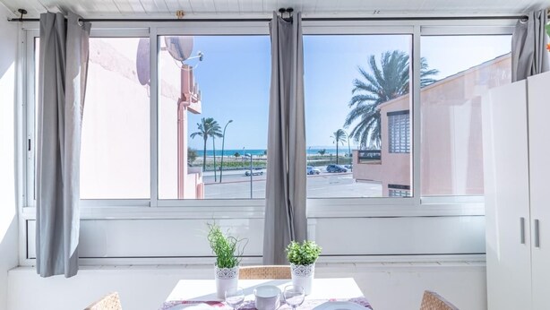 Een kamer met een eettafel gedekt voor twee personen, uitzicht op het strand en een schotelantenne aan de muur.