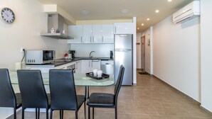 Una cucina moderna con mobili bianchi, un frigorifero in acciaio inossidabile e un'area pranzo con tavolo in vetro e sedie nere.