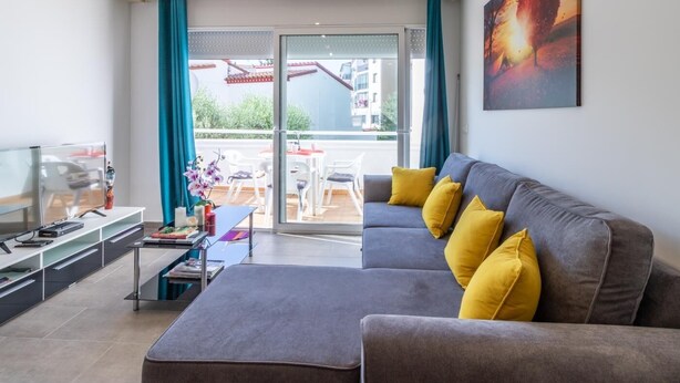 Un soggiorno moderno con un divano grigio, cuscini gialli, una TV a schermo piatto e un'area pranzo con tavolo e sedie.