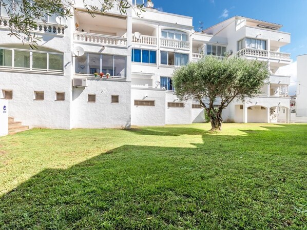 A multi-story residential building with balconies, a grassy courtyard, and a tree.