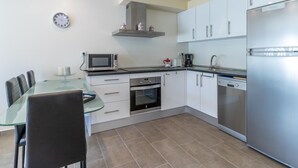 Una cucina moderna con mobili bianchi, un frigorifero in acciaio inossidabile, un forno a microonde e una macchina per il caffè.