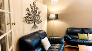 Ein Wohnzimmer mit einem schwarzen Ledersofa, Wandkunst in Form eines Metallbaums, einer Stehlampe und einem Holztisch.