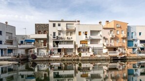 A row of multi-story buildings with balconies, a clear sky, and a calm body of water reflecting the buildings. - Fisherman's house, 4 bedrooms, mooring, WIFI, beach very close. (Empuriabrava)