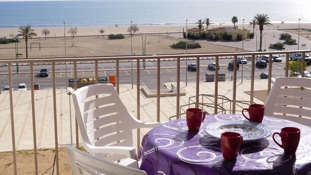 Varanda com uma mesa posta para dois, vista para a praia e um estacionamento.