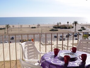 En balkon med et bord dækket til to, med udsigt over en strand og en parkeringsplads.