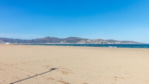Uma extensa praia de areia dourada, com céu azul límpido e montanhas ao longe.