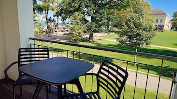 Un balcón con una mesa y dos sillas, con vistas a una zona ajardinada con árboles y un edificio al fondo.
