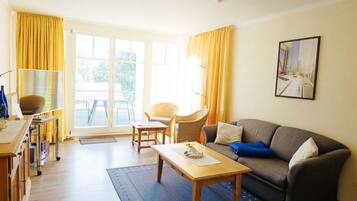 A living room with a sofa, a coffee table, a chair, and a dining area with a cart.