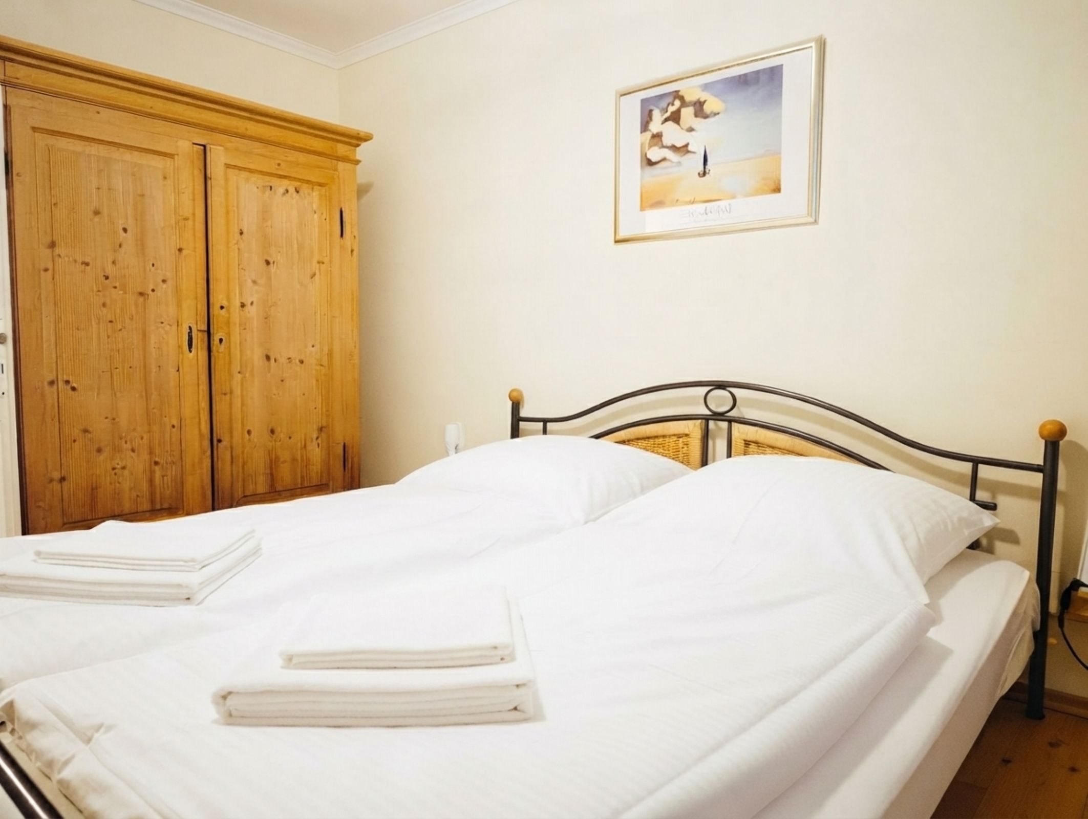 Un dormitorio con una cama doble, armario de madera y un cuadro en la pared.