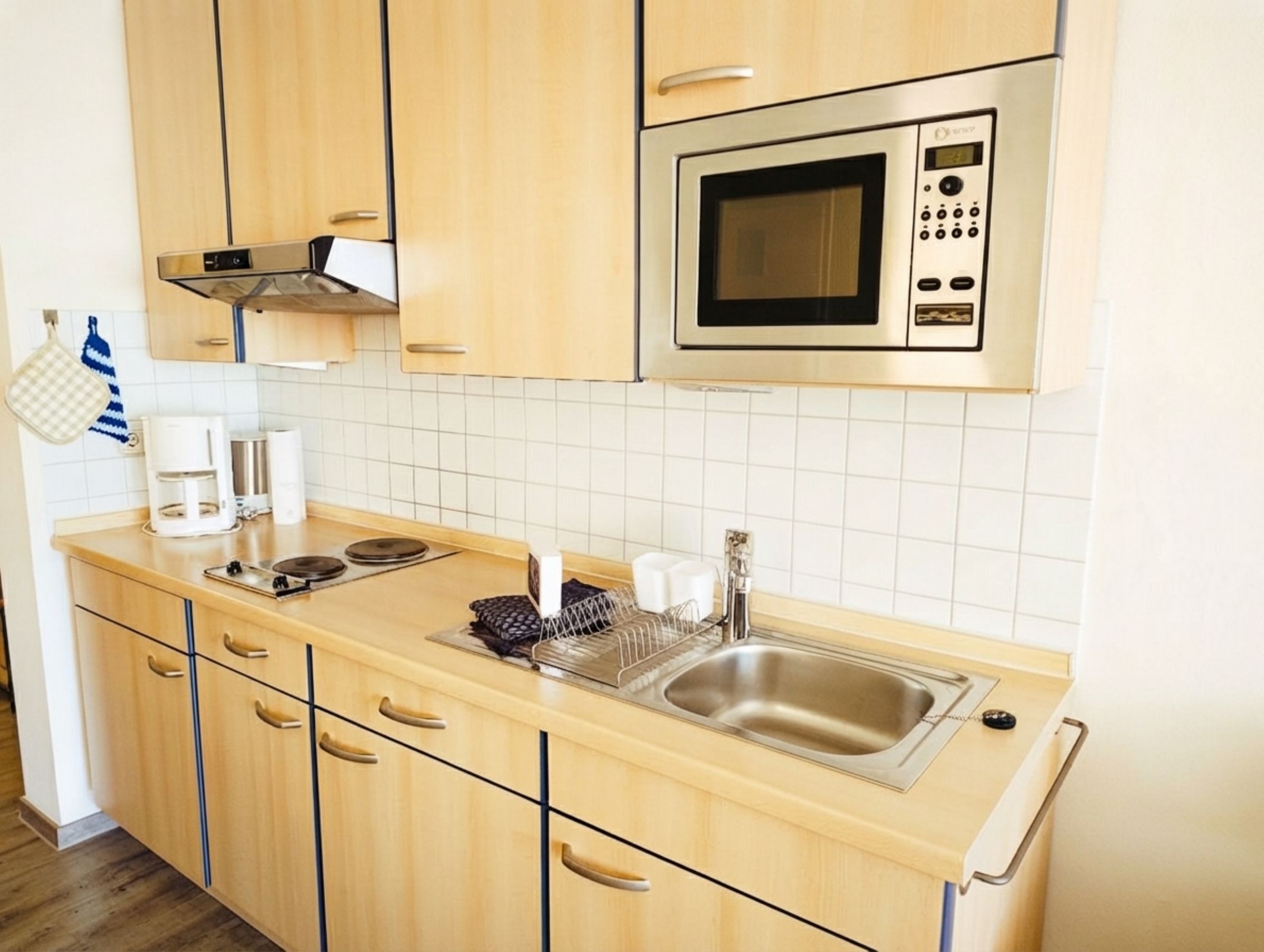 A modern kitchen with wooden cabinets, a stainless steel sink, a microwave, and a coffee maker.