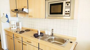 A modern kitchen with wooden cabinets, a stainless steel sink, a microwave, and a coffee maker.
