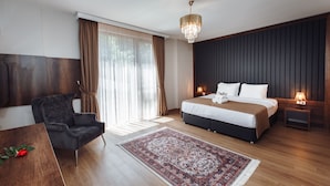 A modern hotel room with a large bed, a dark upholstered chair, a wooden floor, a patterned rug, and a chandelier.