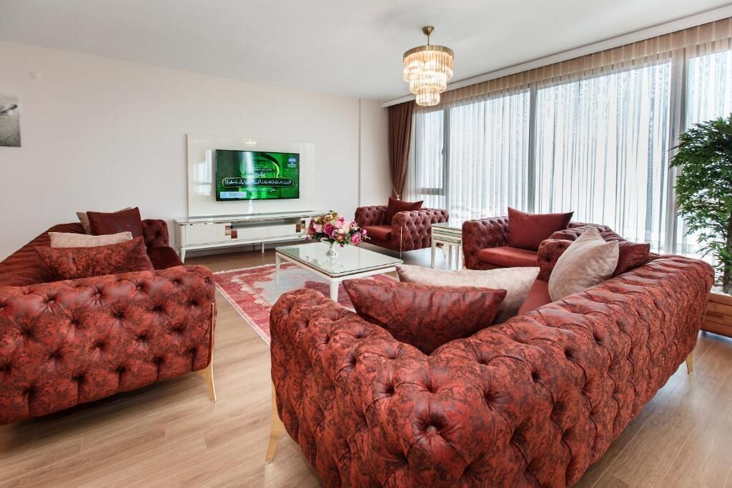 Una sala moderna con un amplio sofá rojo, una mesa de centro de vidrio y un televisor de pantalla plana montado en la pared.