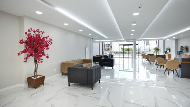 A modern hotel lobby with a marble floor, a large potted plant, and a seating area with sofas and chairs.