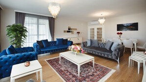 A modern living room with a blue sofa, a grey sofa, a white coffee table, and a chandelier.