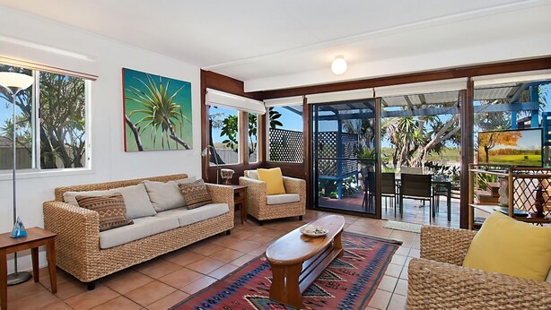 A spacious living area with a sofa, armchairs, and a coffee table, featuring large windows and a view of the outdoors.