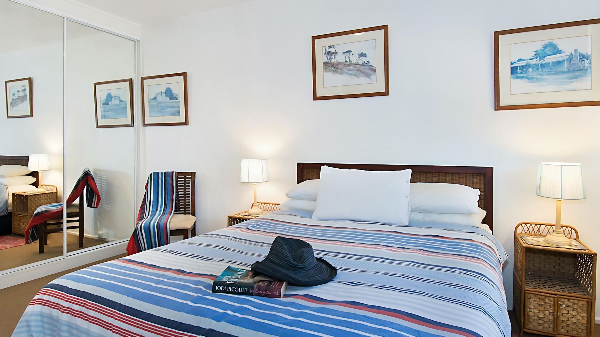 A hotel room with a large bed, two bedside tables with lamps, a chair with a striped blanket, and three framed pictures on the wall.