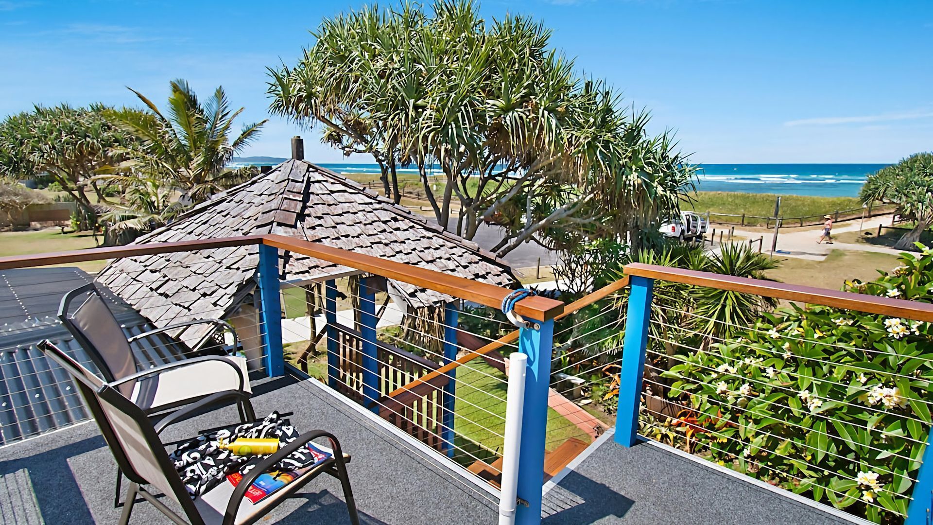 A balcony with a table and chairs, a small hut, and a view of the ocean.