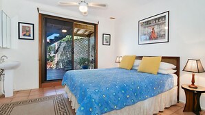 A bedroom with a bed, a nightstand, a lamp, a window, and a door leading to a balcony.