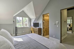 Ein Schlafzimmer mit einem großen Bett, einem Fernseher auf einer hölzernen Kommode und einem Fenster mit Blick auf Grünflächen.