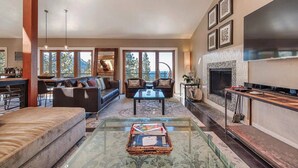 A spacious living room with a large TV, a fireplace, and a dining area with a view of the outdoors. - Skylake Serenity Retreat (Incline Village)